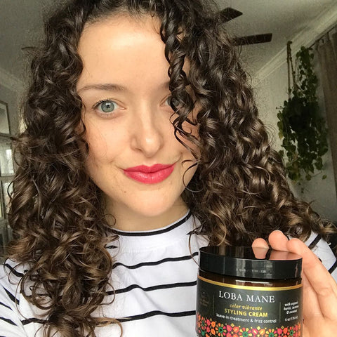 Woman with beautiful curly hair and red lipstick smiling and holding Loba Mane's Styling Cream