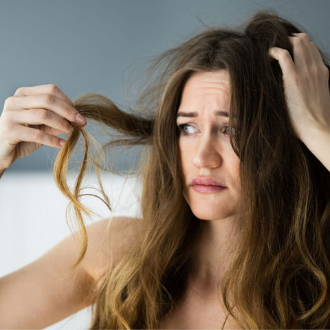 Woman with long frizzy hair, holding up a piece of it and looking frustrated.