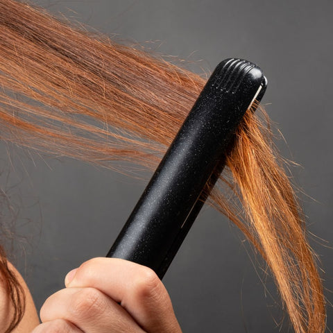 Person with dyed hair using a flat iron on their hair.