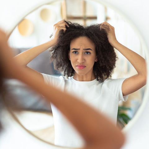 Woman looking into a mirror and tugging at her curly hair while frustrated.