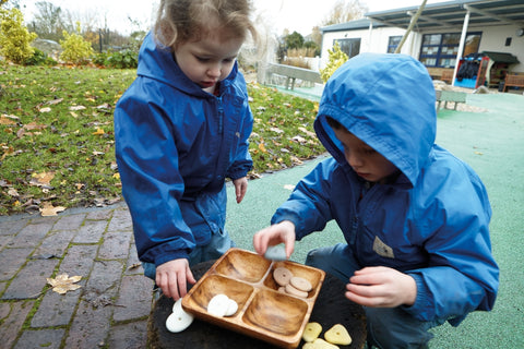 An photo of 2 children playing with threading pebbles