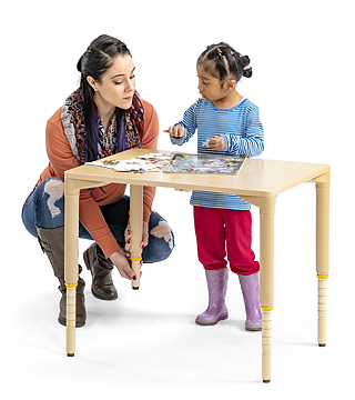 teacher adjusting height legs on classroom table as kindergarten child waits