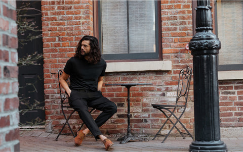 smartly dressed man sitting at a table and chairs outside