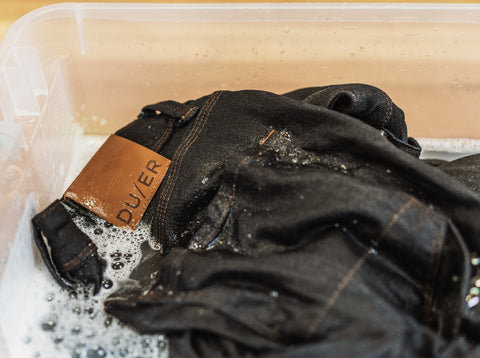 A pair of DUER denim being soaked in a container