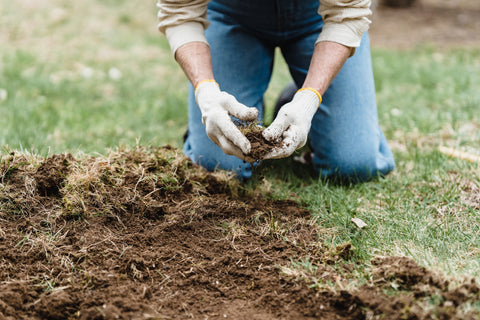 A person working outside in dirt and grass wearing denim