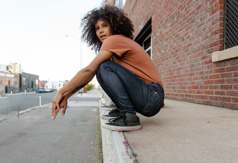 Woman wearing DUER denim crouching on a sidewalk