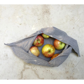 Gray cotton bento bag with long tie-able ends lays open on a marble countertop with reddish, yellow apples inside.