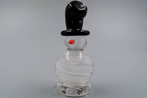 A single glass snowman figure with a tall, crooked, black top hat and an orange nose. The snowman's body is made of a swirl of clear and white glass, its head is clear glass. 