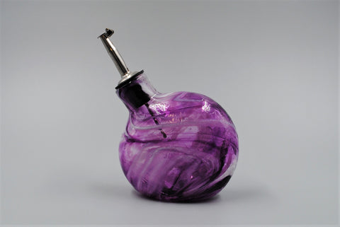 A single purple handmade glass oil bottle, shown with its stainless steel spout facing to the left. 