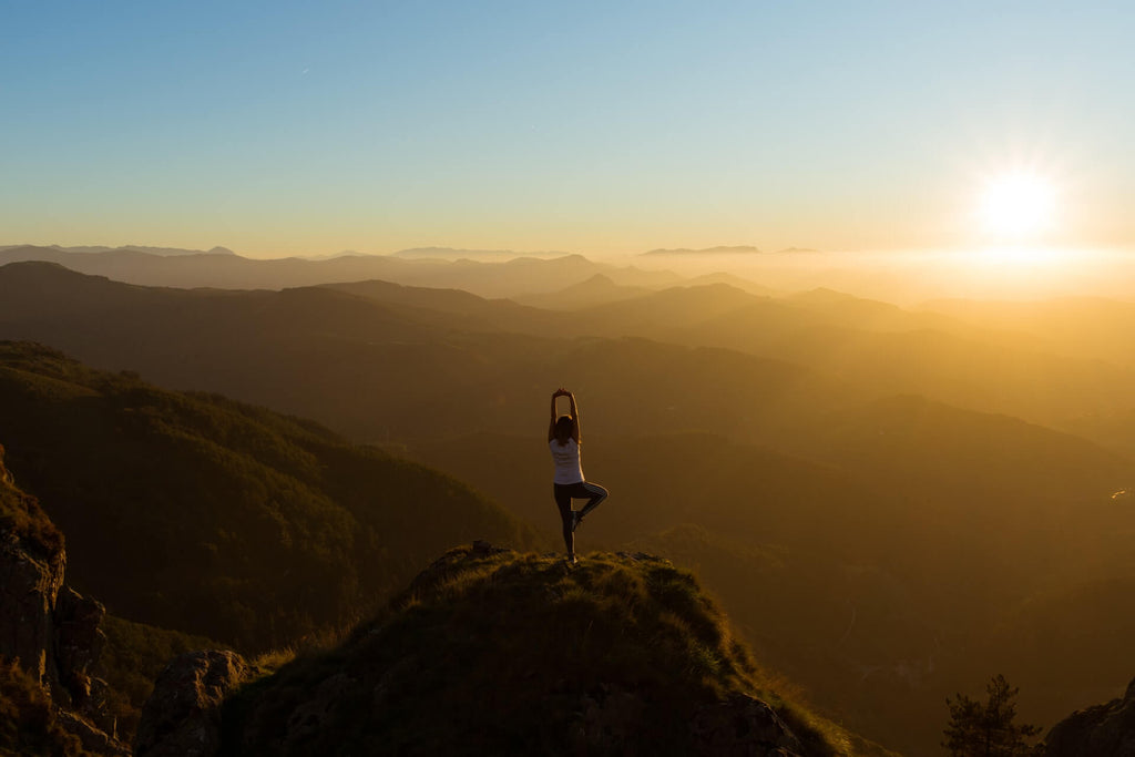 woman standing on a hill landscape doing a yoga pose