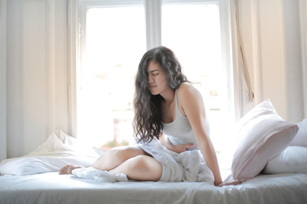 woman sitting on bed hand on her stomach looking ill