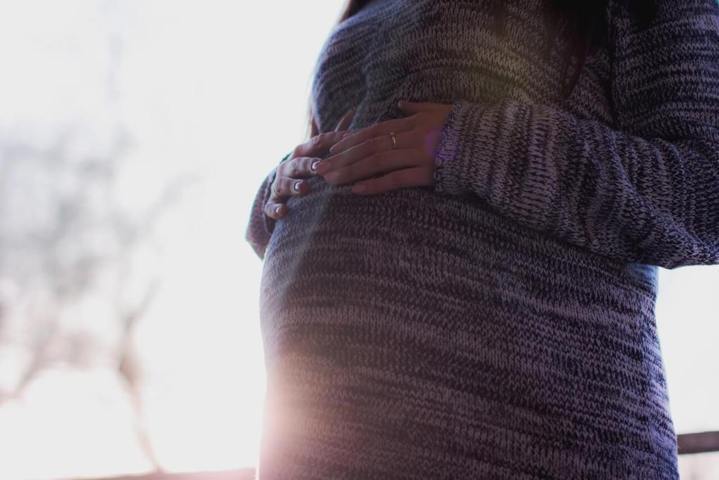 pregnant woman holding her belly sunrays behind her