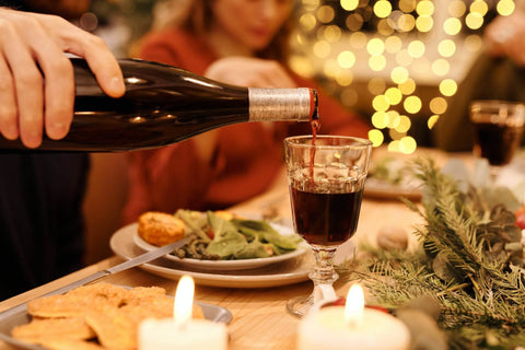 man's hand pouring red wine in a wineglass on a dinner table