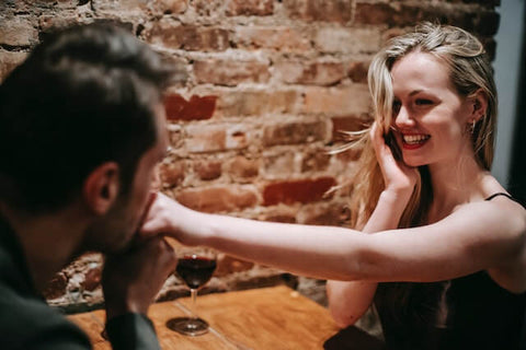 man kissing a woman's hand with a glass of wine on the table