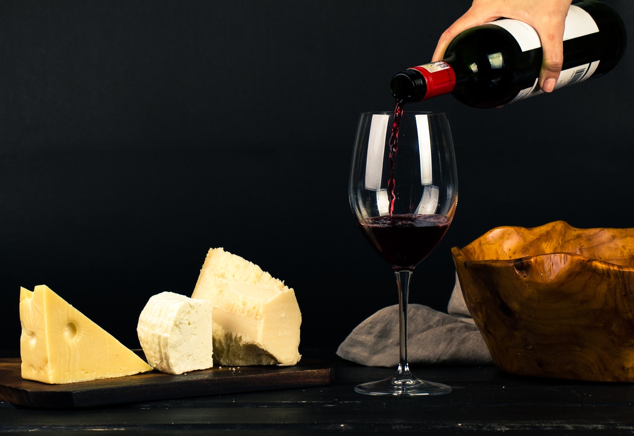 3 different slices of cheese and bottle of red wine being poured in a glass