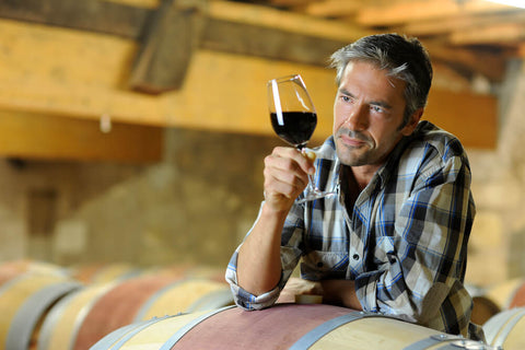 man leaning on a wine barrel looking at a wine glass