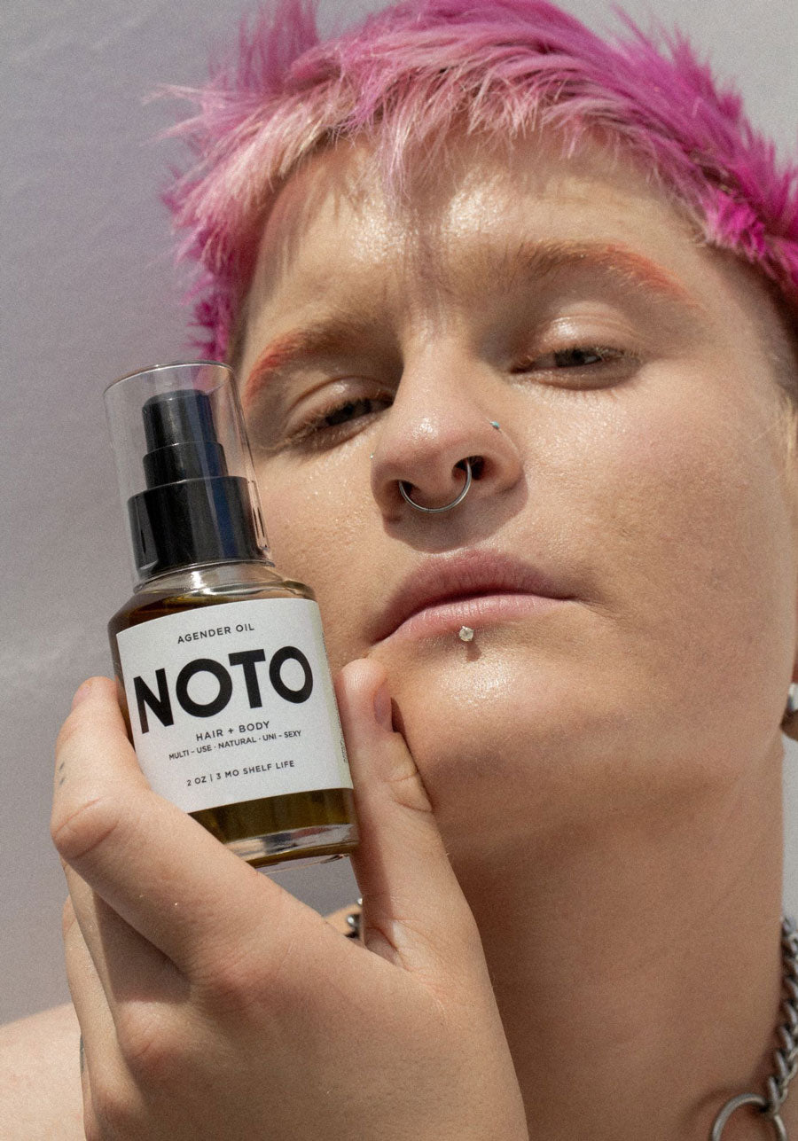 A genderqueer person holding NOTO Agender Oil