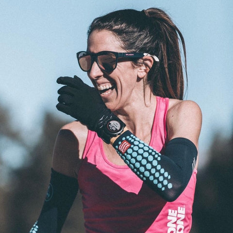 Steph Bruce wearing sunglasses, a pink tank top, black arm sleeves and cotton gloves laughs after a workout