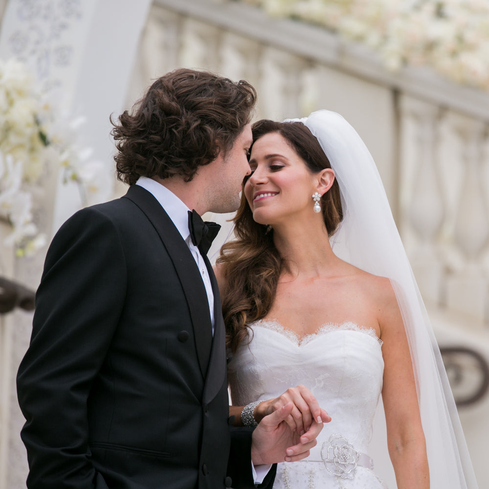 Bride and groom share an intimate moment of affection as friends and family celebrate their marriage. Bride wears a Valerie Beverly Hills long wearing lip stain in Jill.