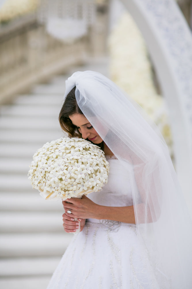 Bride holds bouquet of white flowers with veil over face