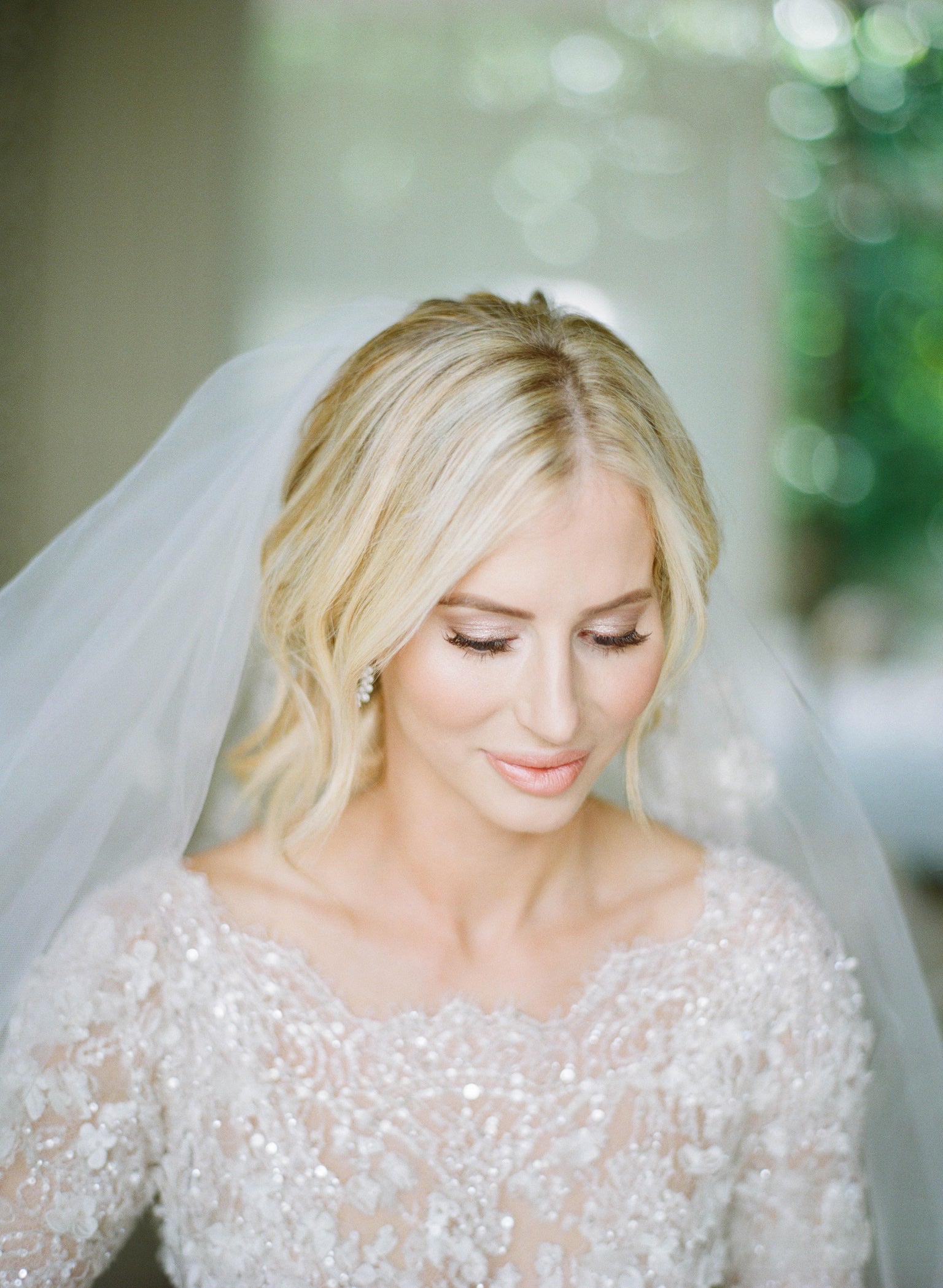 Bride looks down to show off her soft rose gold eyes, false warm brown lashes and glossy peach lips. Makeup by Valerie.