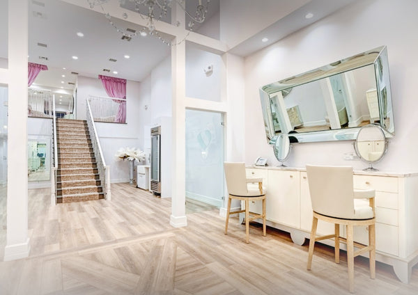 A service area where brows, makeup, and waxing are performed. Two high chairs and multiple mirrors. A staircase that leads to private services can be seen in the back.