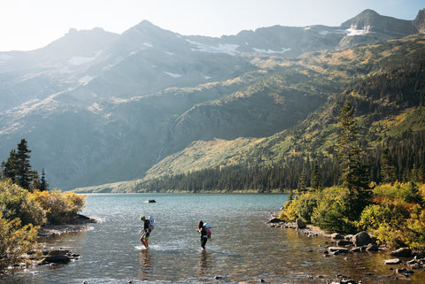 two people walking through a lake on a hike in the mountains