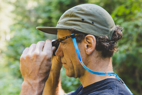 man with sunnystring sunglass string putting on sunglasses whilst on a hike