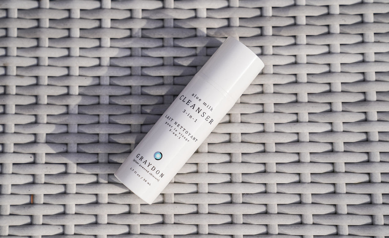 A bottle of soothing milk cleanser for sensitive skin lying on an off-white rattan surface.