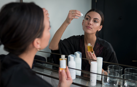 Brunette woman applying Superfood Serum in mirror