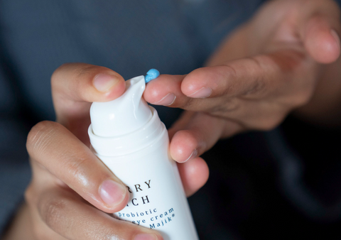 Close up of woman's hands pumping a small amount of bright blue Graydon Skincare Berry Rich Face + Eye Cream onto finger.