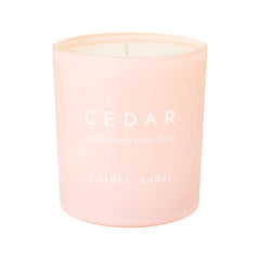 A natural, GMO-free soy candle scented with essential oils of Texas cedarwood and Madagascar ylang ylang and housed in luxe, pale pink glass with hand stamped white text against a white background.