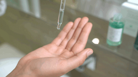 A close-up GIF of an aquamarine-coloured facial serum being dispensed into the palm of a woman's hand with a bottle of Fullmoon Serum in the background