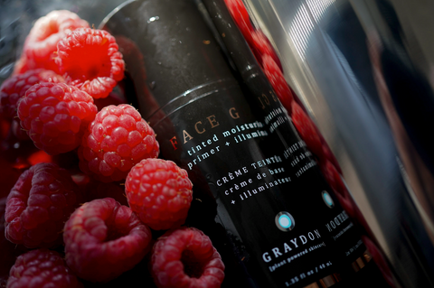 Bottle of Graydon Skincare Face Glow laying next to ripe, red raspberries.