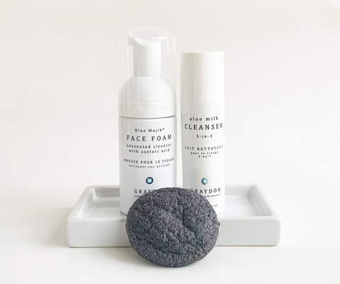 Bottle of Graydon Skincare Face Foam Cleanser and Aloe Milk Cleanser on white soap dish with Bamboo Charcoal Sponge in front.