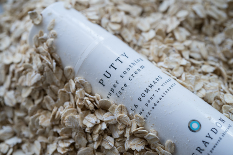 Bottle of Graydon Skincare Putty moisturizer laying in oats