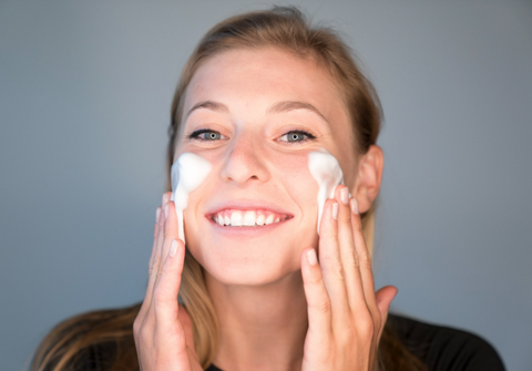 Young woman smiling and applying Graydon Skincare Face Foam cleanser to cheeks.
