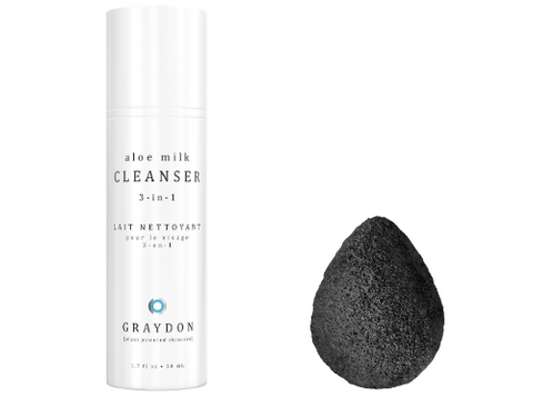 A bottle of soothing cleanser for sensitive skin next to a black konjac sponge for sensitive skin against a white background