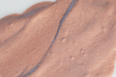 A smear of tinted moisturizing skin primer with iridescent mica against a white background 