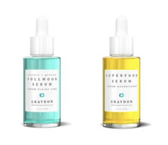 A glass bottle of aquamarine-coloured retinol alternative face serum next to a glass bottle of gold-coloured hydrating serum for dry skin against a white background