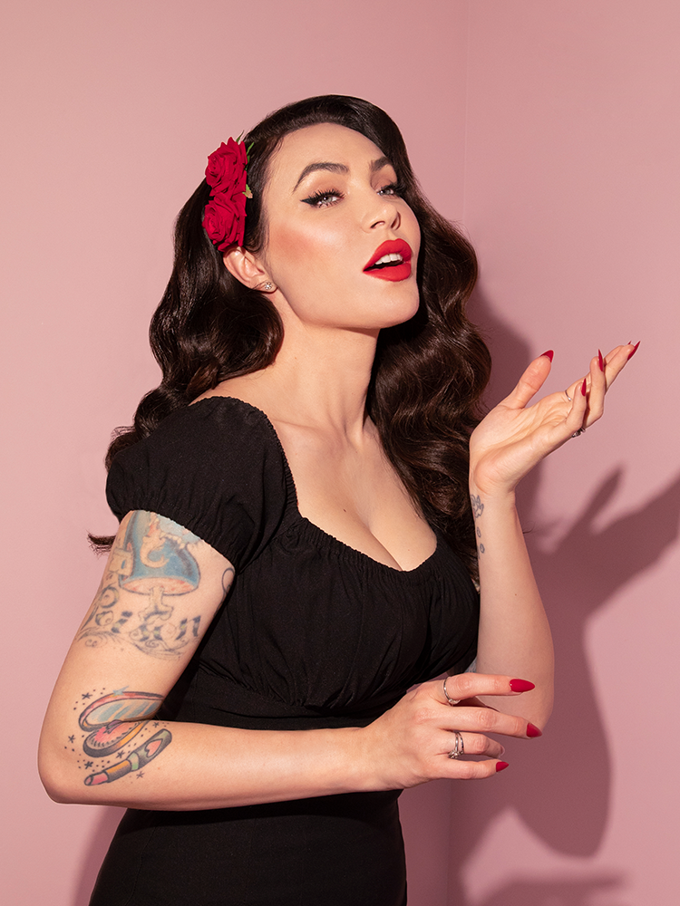 Micheline Pitt posing with her hand outstretched to the air while wearing the Vintage Double Red Rose Hair Comb. 