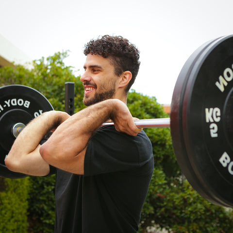 Brunette man smiling while holding barbell to chest