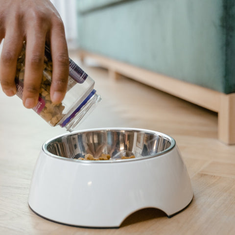 A hand pouring food into a white bowl