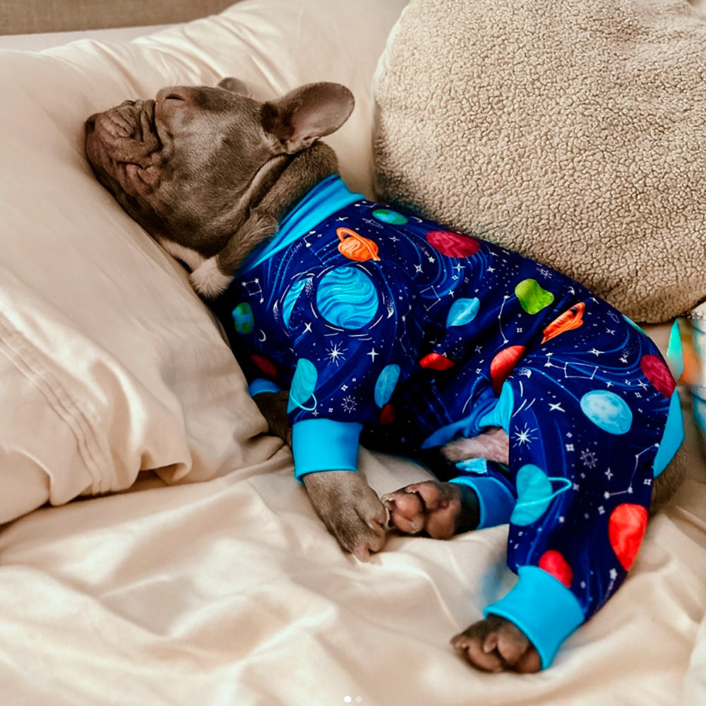 A small dog comfortably sleeping on a bed while wearing colorful Sparkpaw's pajamas