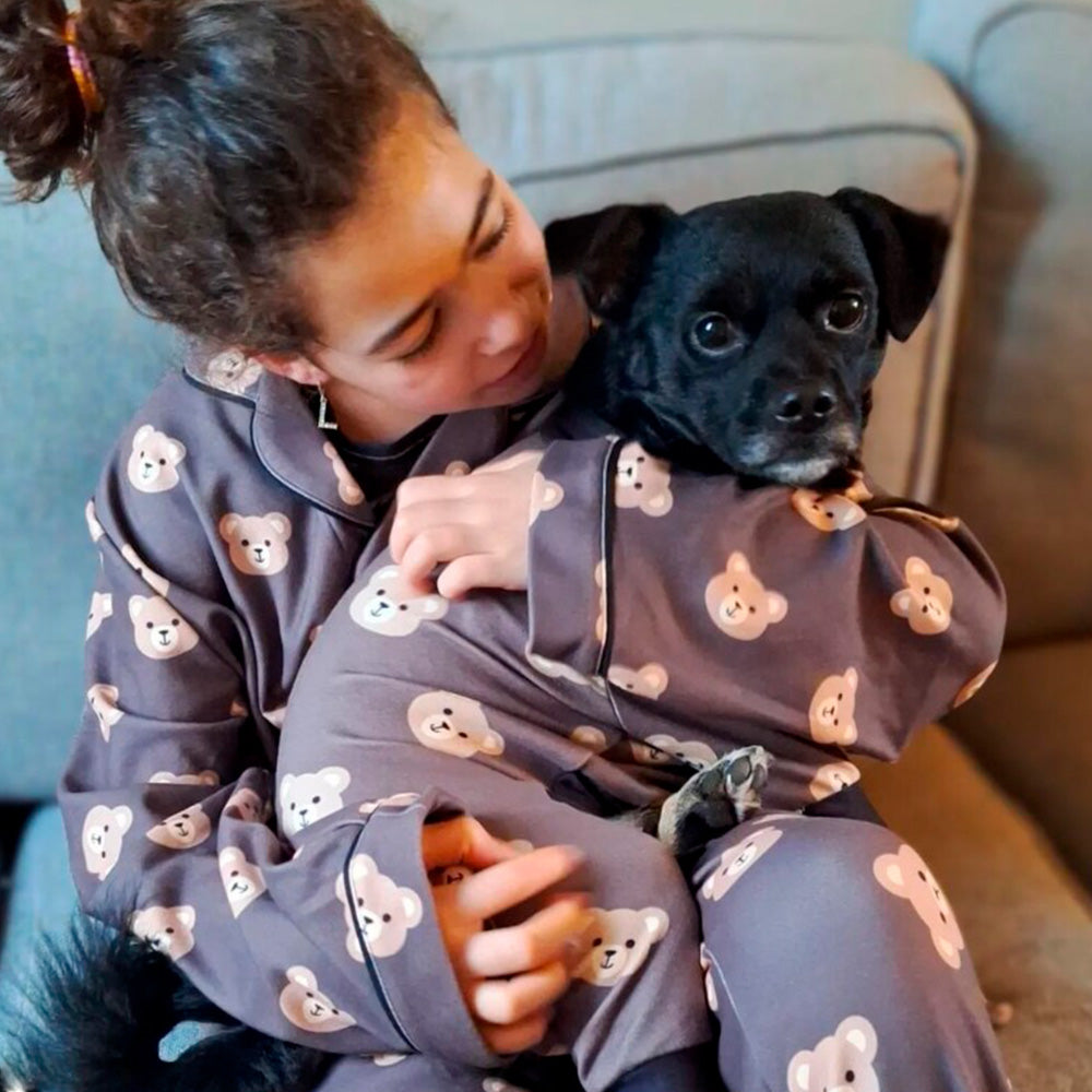 A young lady sitting on a couch wearing matching pajamas lovingly holding her small black dog