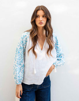 female wearing white linen blouse with light blue embroidery on the sleeves on white wall