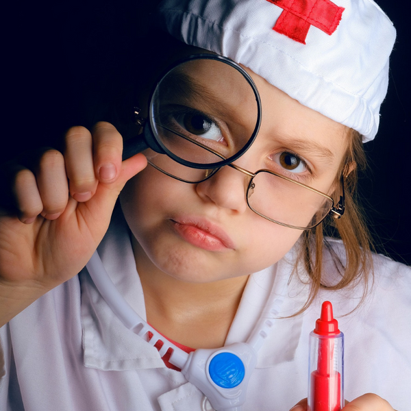 little girl dressed up as a doctor looking through a magnifying glass