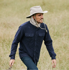 man walking through a field wearing a fishing hat with a neck flap and chin strap.