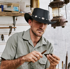 Man wearing an Australian leather hat with metal details, sharpening tools.