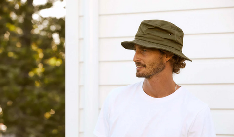 Man wearing a white t-shirt and a green bucket hat looks into the distance.